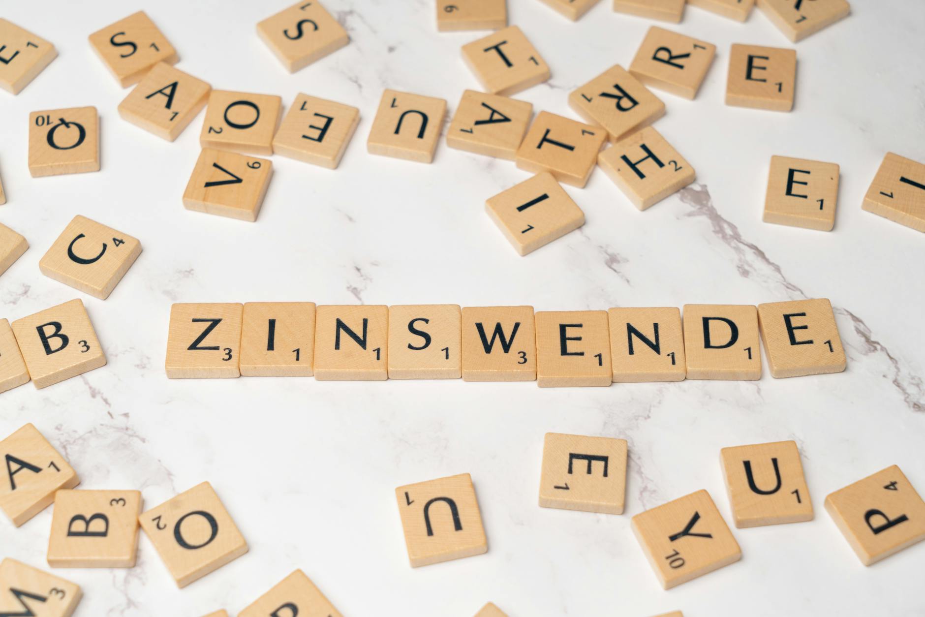 Scrabble tiles arranged to spell 'Zinswende' on a marble surface with scattered tiles around.